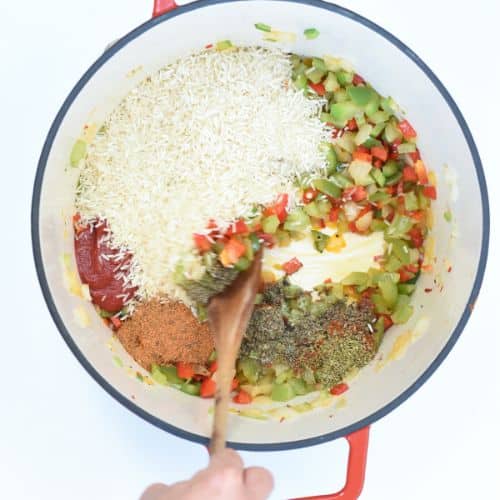 Rice and tomato paste added to cooked vegetable in a cast-iron pan.