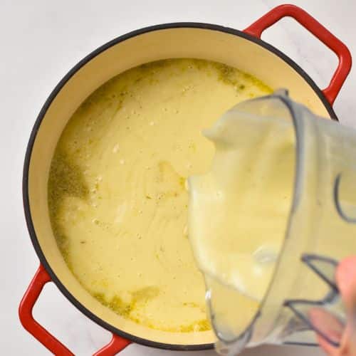 Pouring blended vegan potato soup in cast-iron pan.