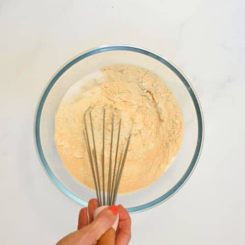 Stirring dry vegan protein pancake ingredients in a mixing bowl.