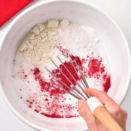 Stirring dry vegan strawberry cake ingredients in a large mixing bowl.