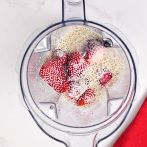 Strawberries and soy milk in the jug of a blender.