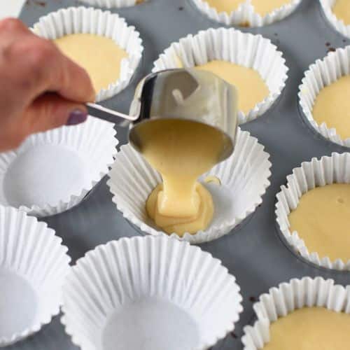 Pouring vegan cupcake batter into a muffin tin lined with cupcake liners.