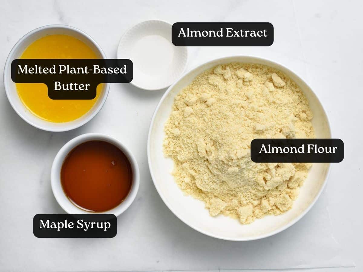 ingredients for almond flour cookies in bowls: almond flour, maple syrup, melted plant-based butter, and almond extract