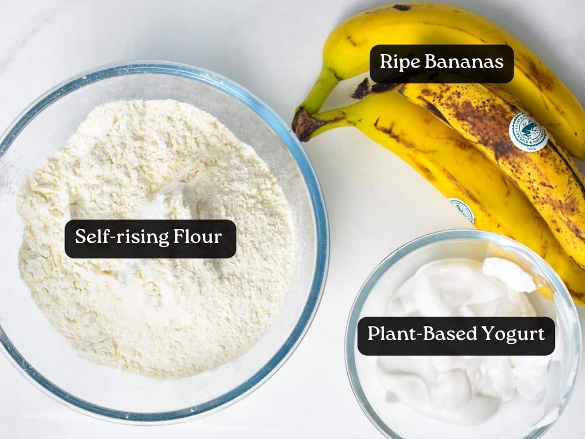 Ingredients for Banana Scones on a work surface, a bowl with self-rising flour, a bowl with plant-based yogurt, and ripe bananas