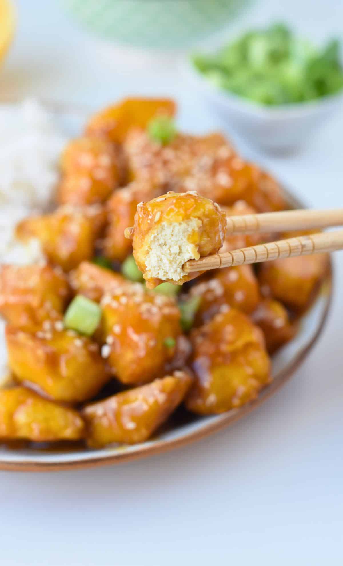 Orange tofu piece held in chopsticks.