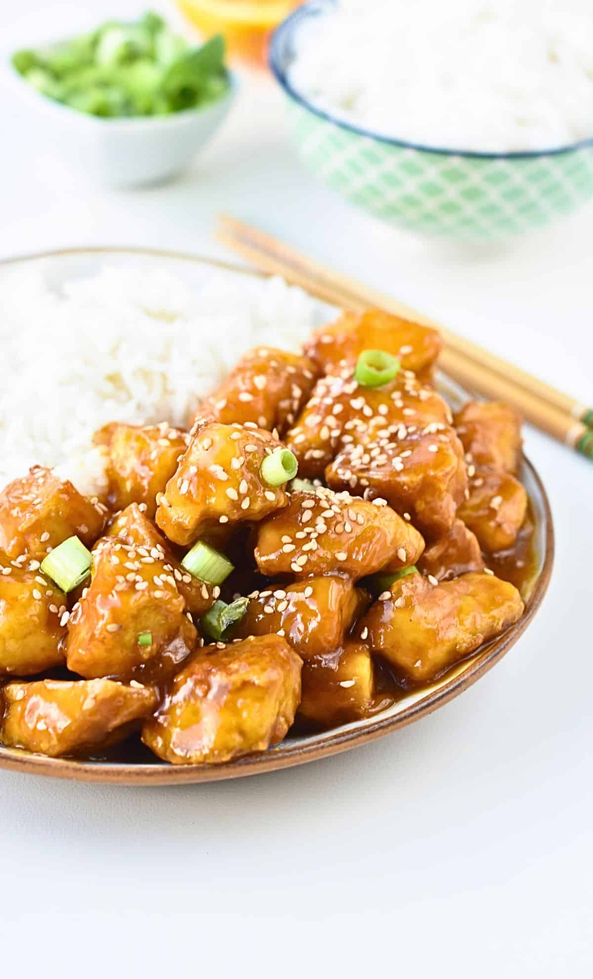 Crispy orange tofu pieces on a plate with white rice.