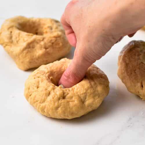 a thumb pressing the center of a donut dough to form the hole