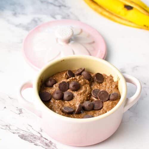 a light pink ceramic mini casserole filled with protein mug cake batter and chocolate chips on top, unbaked