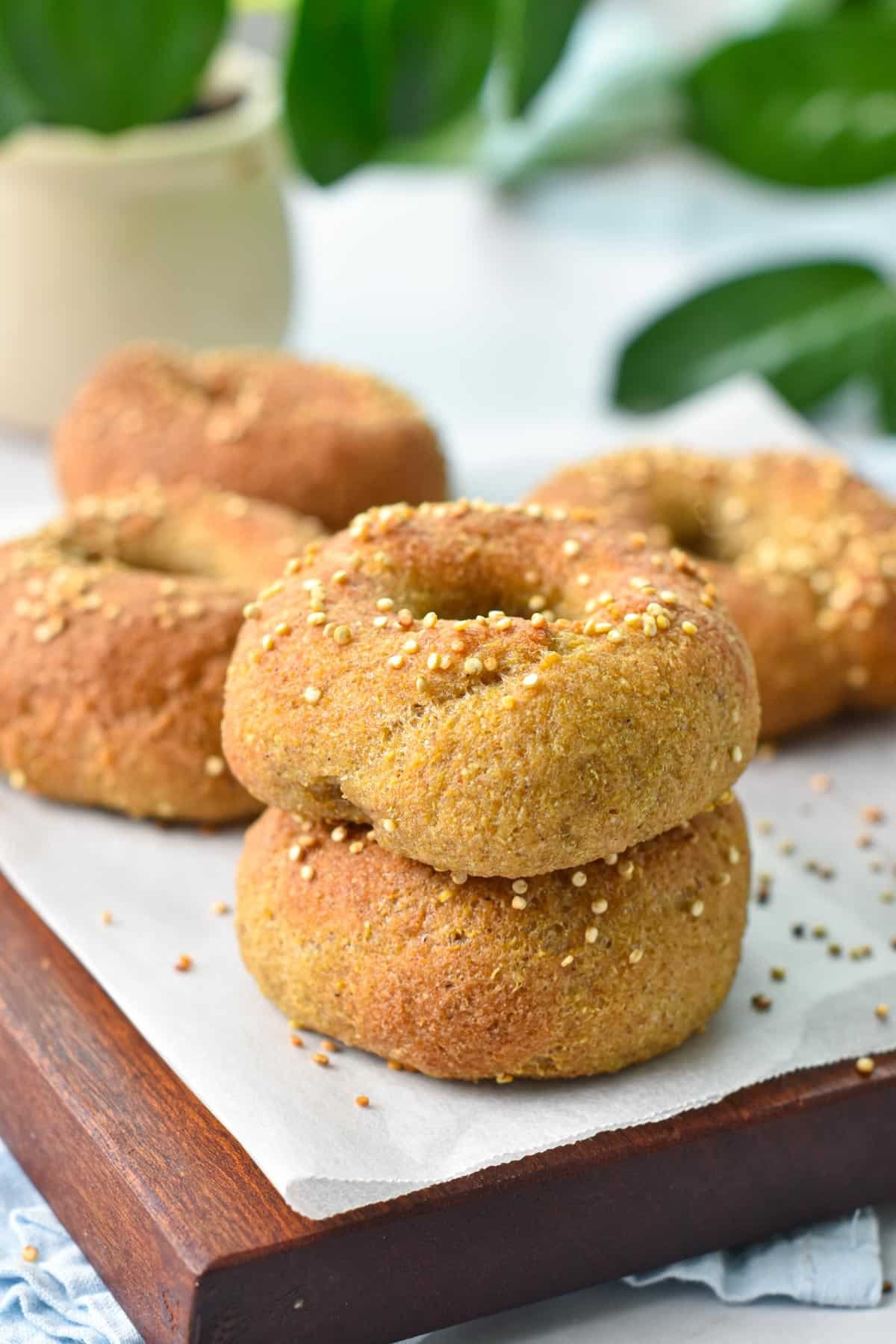 A stack of two quinoa bagels in front of more bagels on a chopping board.