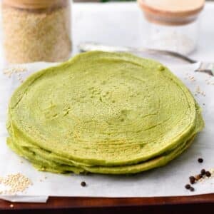 a stack of spinach quinoa tortillas on a wooden chopping board covered with white parchment paper