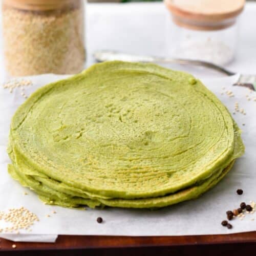 a stack of spinach quinoa tortillas on a wooden chopping board covered with white parchment paper