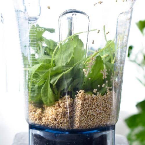 a blender jug filled with soaked quinoa, spinach and water