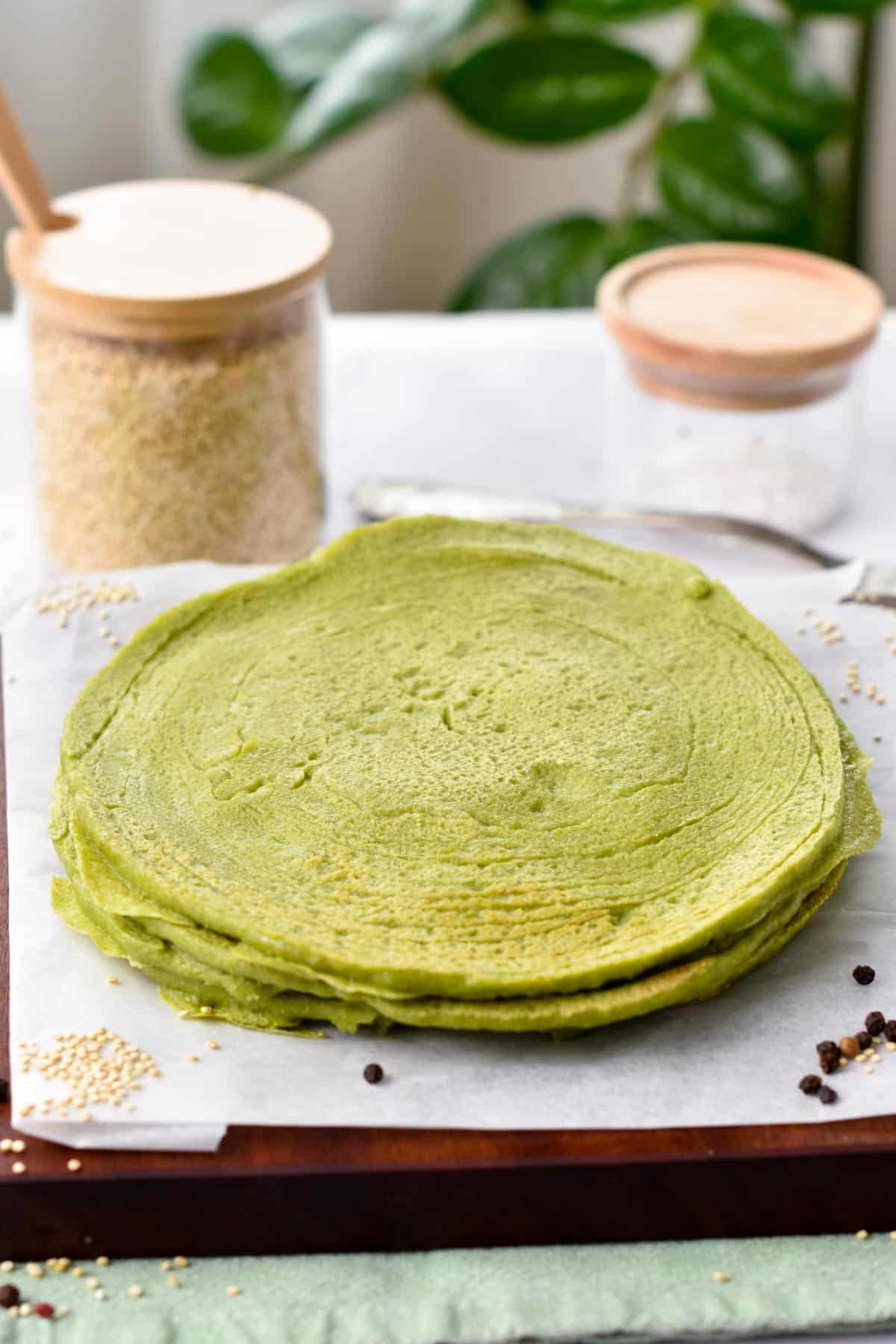 A stack of spinach quinoa tortillas on a wooden chopping board covered with white parchment paper.