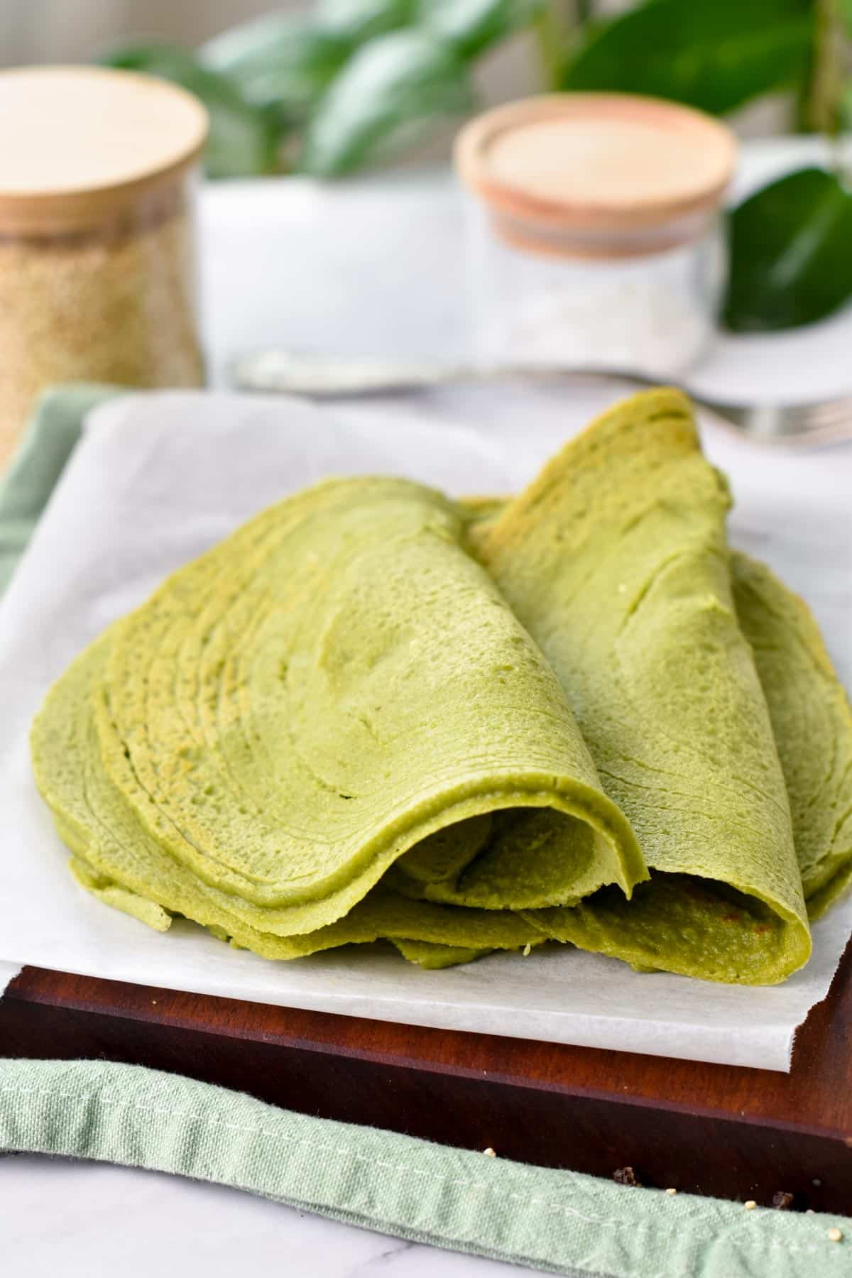 Two spinach quinoa tortillas folded half way on a wooden chopping board covered with parchment paper.