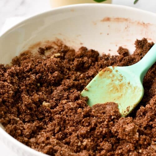 A bowl filled with vegan chocolate shortbread batter made with almond flour and a light green rubber spatula in the bowl.