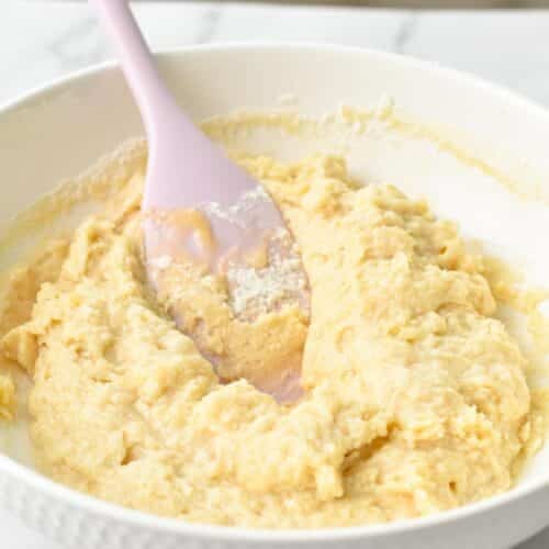 a bowl filled with yogurt cake batter and a pink rubber spatula