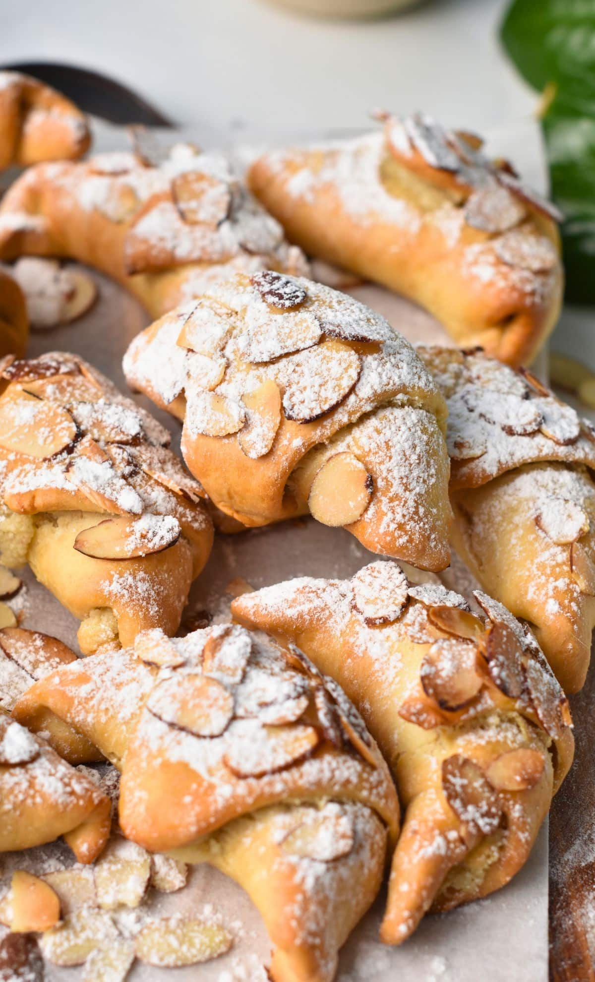 Almond Croissant Pastry stacked on a baking sheet and covered with almond slices and powdered sweetener.