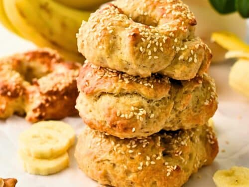 Banana Bagels stacked in front of a bunch of bananas.