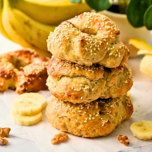 Banana Bagels stacked in front of a bunch of bananas.