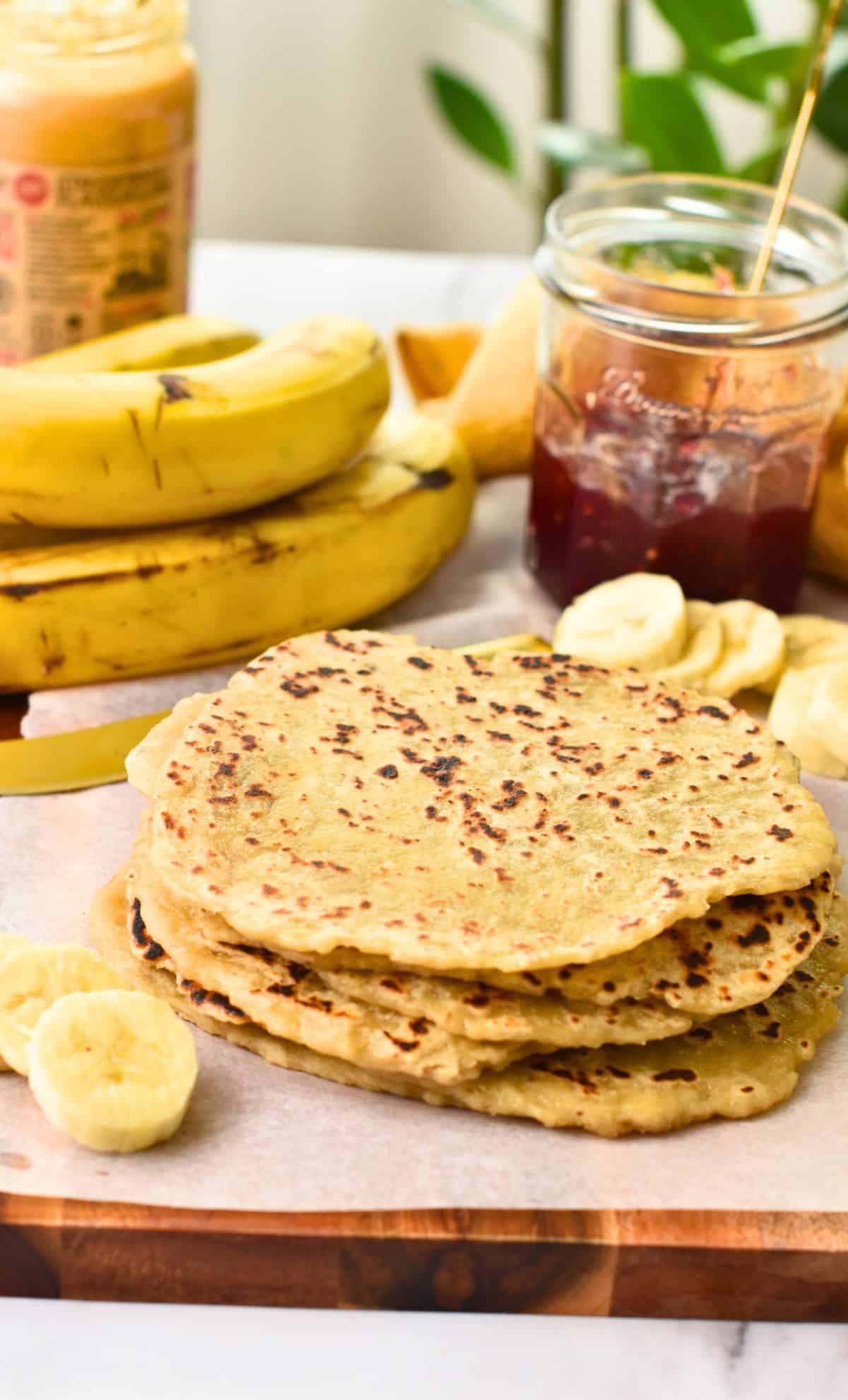 Banana Tortillas stacked on a wooden board with toppings around it.