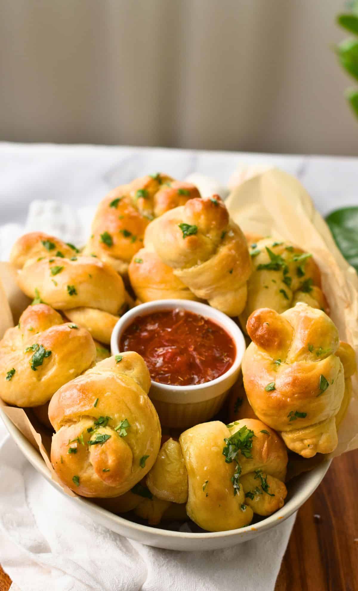 Garlic knots around a ramekin with tomato sauce.