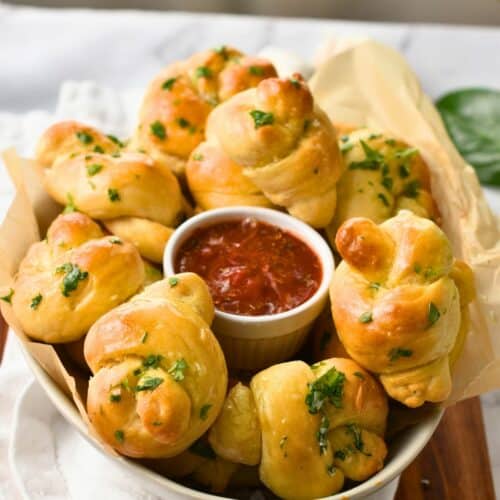 Garlic knots around a ramekin with tomato sauce.