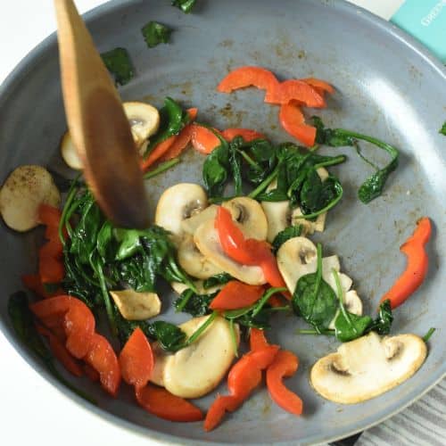 Stir-frying vegetables in a frying pan for the vegan omelette.