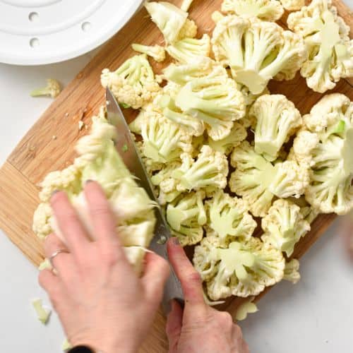 Chopping cauliflower into florets on a chopping board.