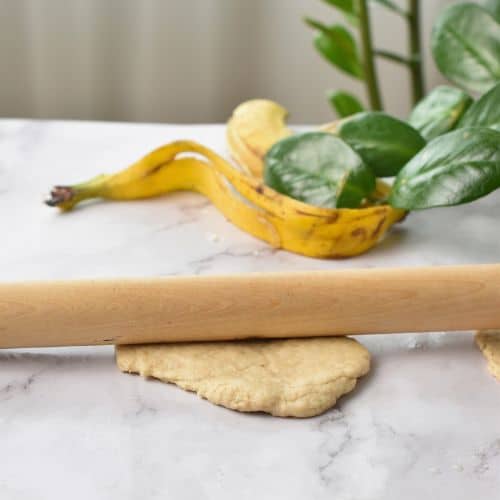 Rolling banana tortilla dough with a rolling pin.