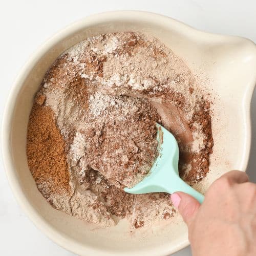 Chocolate Protein Muffins dry ingredients in a mixing bowl stirred with a silicone spatula.