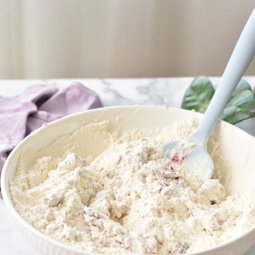 Combining purple sweet potatoes with flour in a bowl with a silicone spatula.