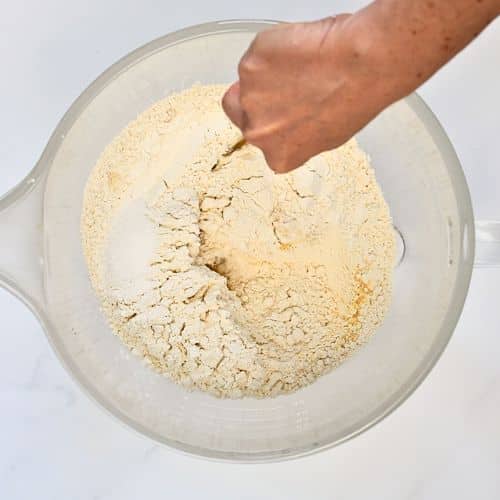 Stirring dry spelt flour pizza dough ingredients in a mixing bowl.