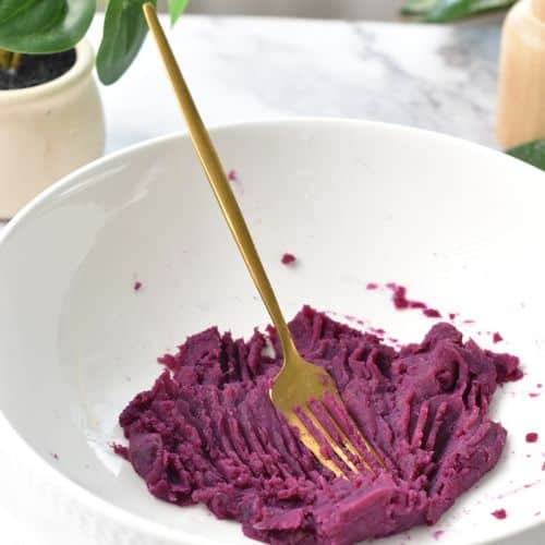 Purple sweet potato puree in a mixing bowl with a golden fork.