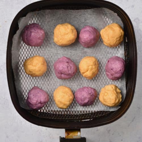 Purple and orange sweet potato donut holes in the basket of an air fryer.