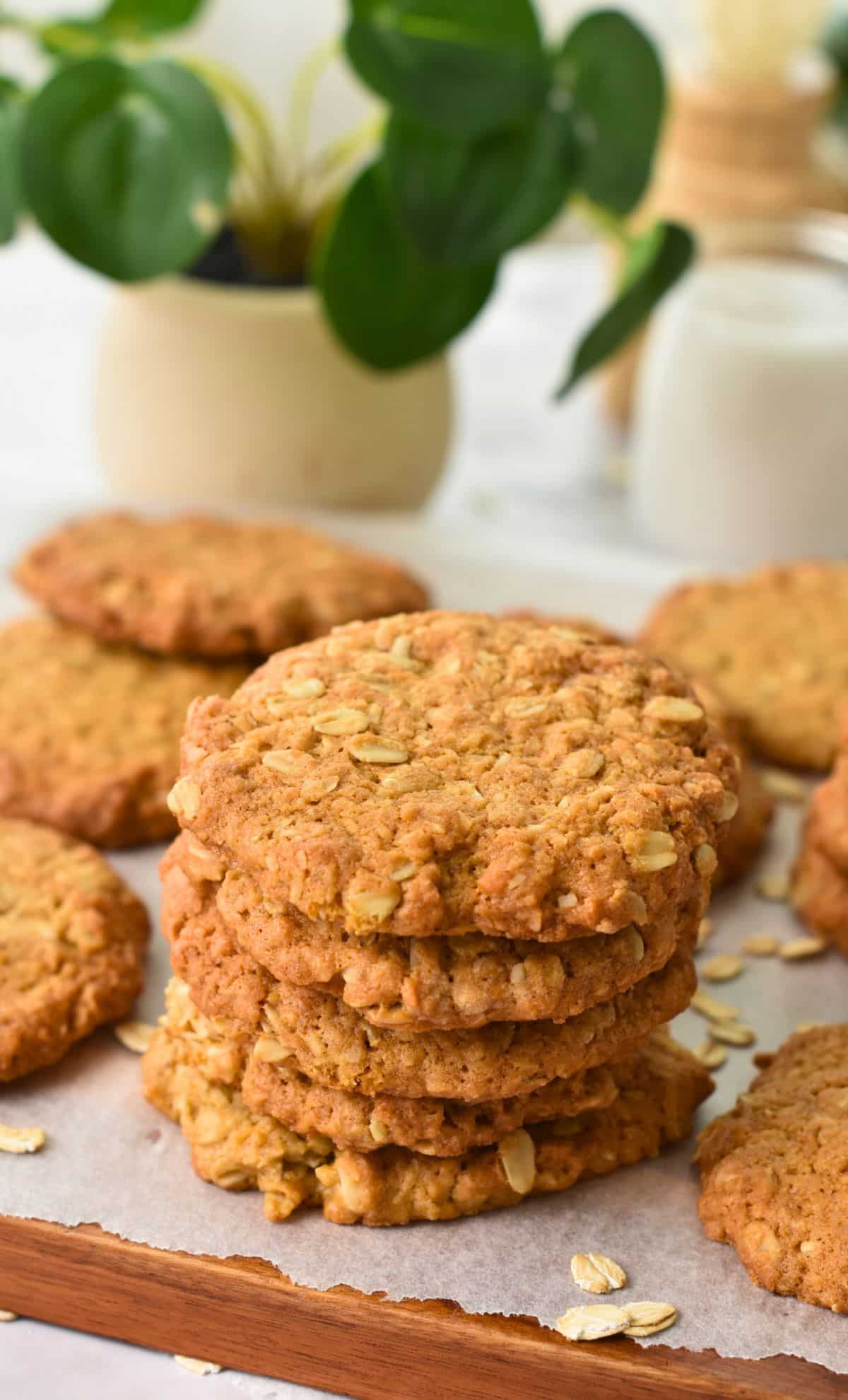 Vegan Anzac Cookies stacked on a wooden board with parchment paper.