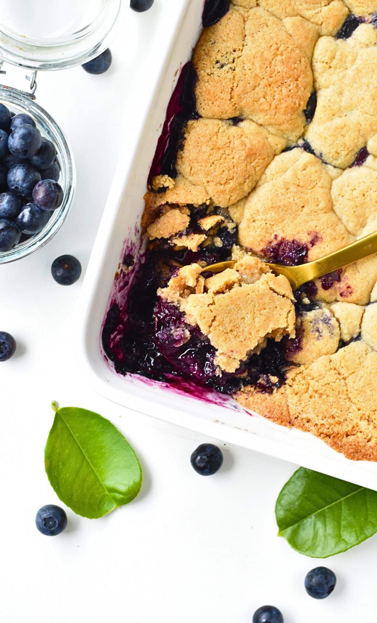 Vegan Blueberry Cobbler in a large ceramic pan with a golden spoon.
