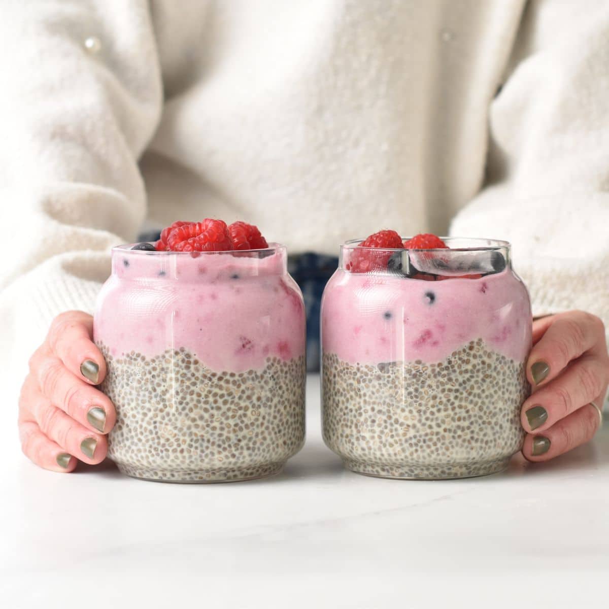 High Protein Chia Pudding in two jars, decorated with raspberries and blueberries.