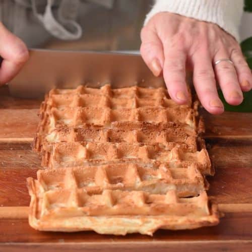 Slicing Banana Churros Waffles with a kitchen knife on a wooden board.