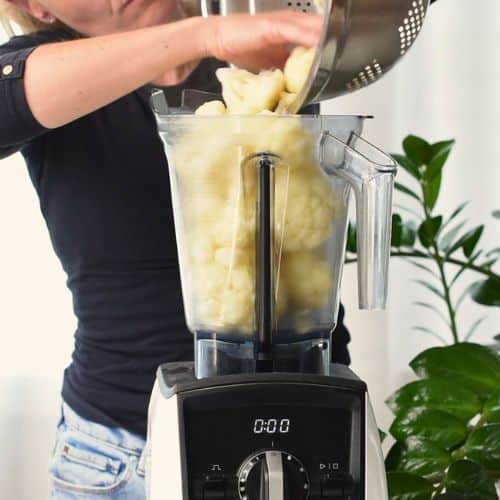 Pouring cooked cauliflower in a blender.