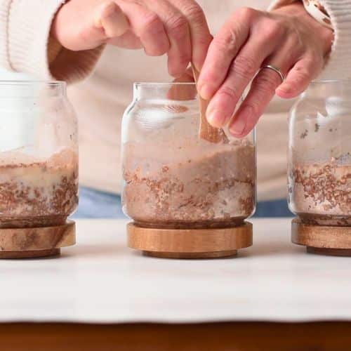 Stirring milk into Three jars with Chocolate Peanut Butter Protein Overnight Oats