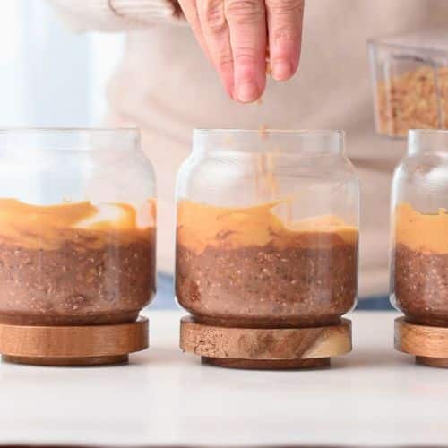 Adding toppings to Three jars with Chocolate Peanut Butter Protein Overnight Oats