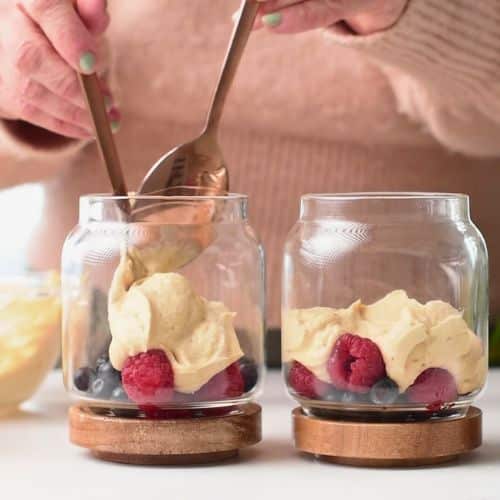 Pouring some yogurt protein powder mix on top of fresh berries in a glass jar.