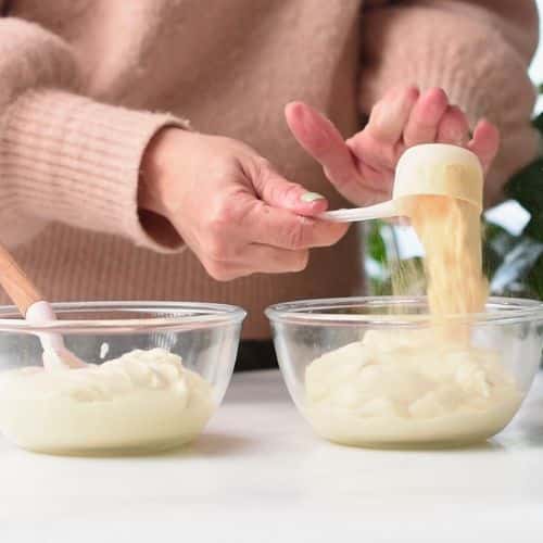 Pouring protein powder on plant-based yogurt in a glass bowl.