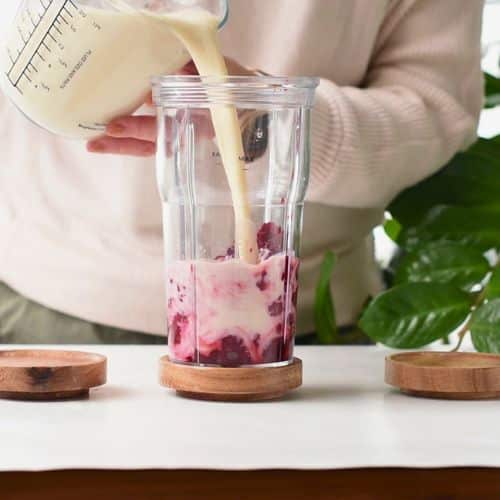 Pouring soy milk on thawed berries in a blender.