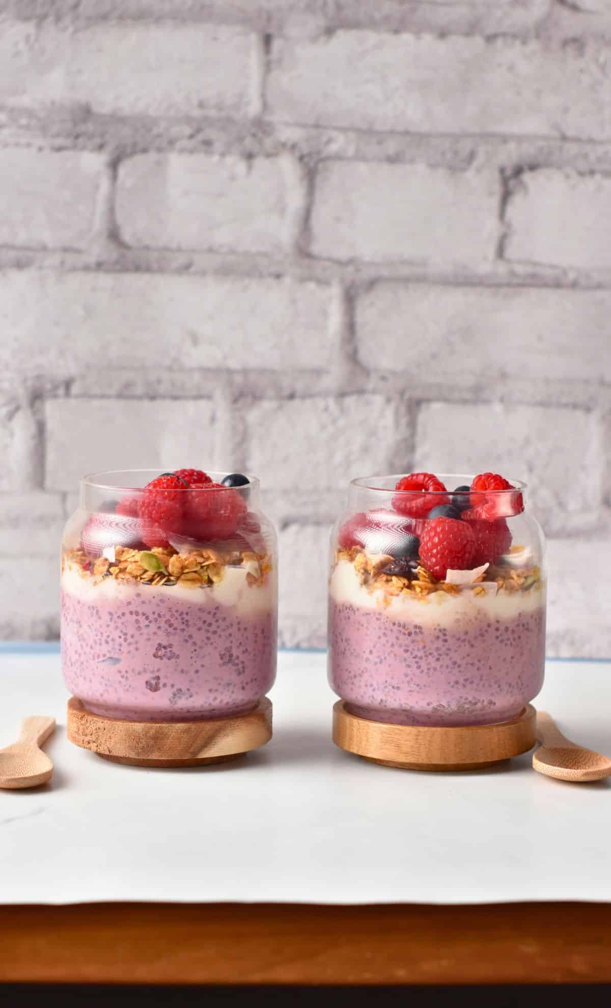 Two jars of Raspberry Chia Pudding decorated with fresh berries.