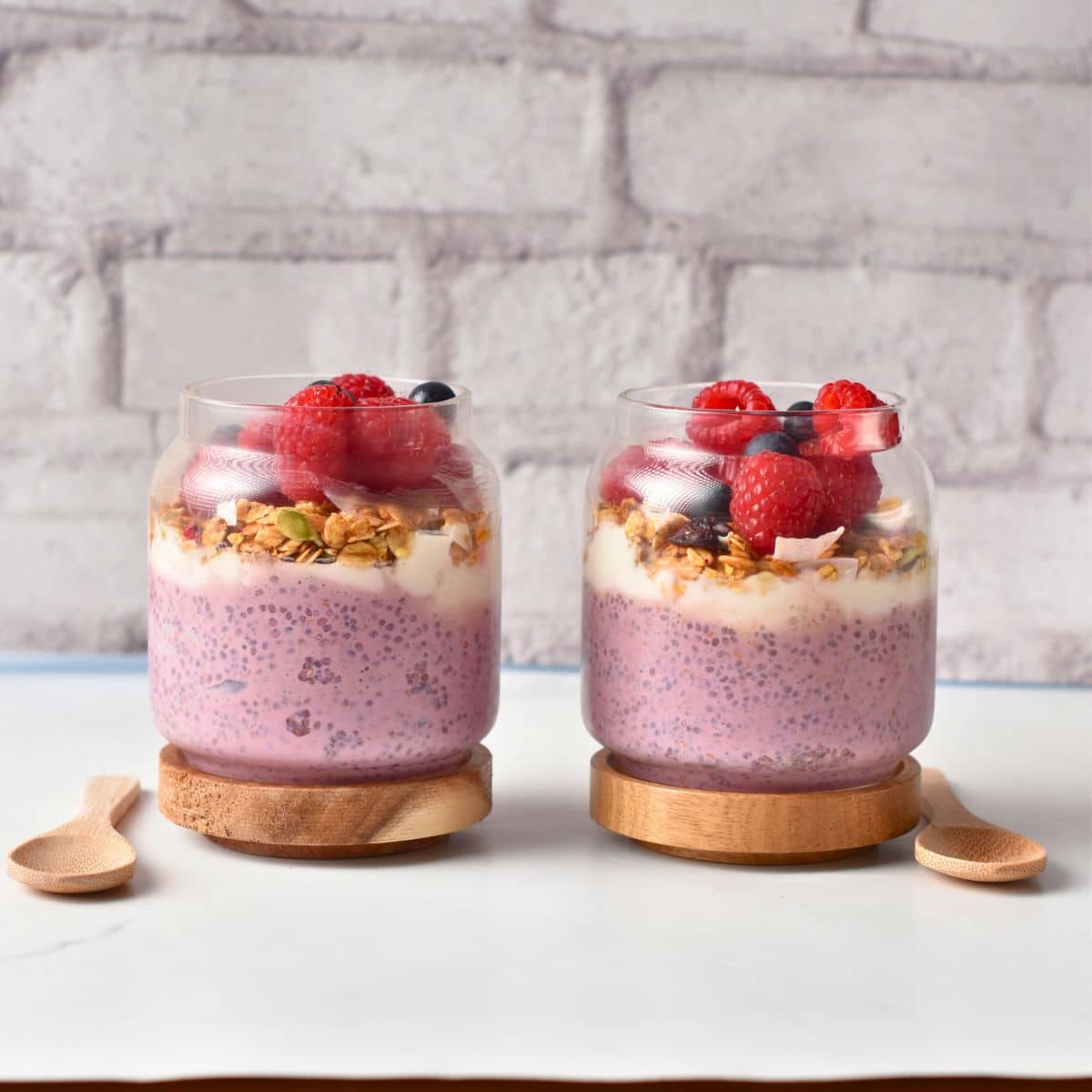 Two jars of Raspberry Chia Pudding decorated with fresh berries.