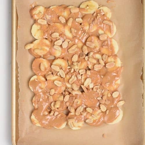 Adding peanut butter and crushed peanuts on the banana slices.