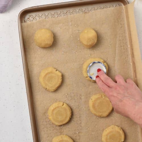 Flattening the cookies with a lid on a baking sheet.