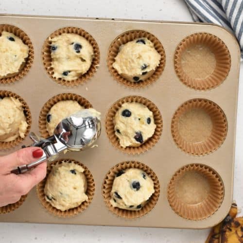 Transferring the Healthy Banana Blueberry Muffin batter in a muffin tin.