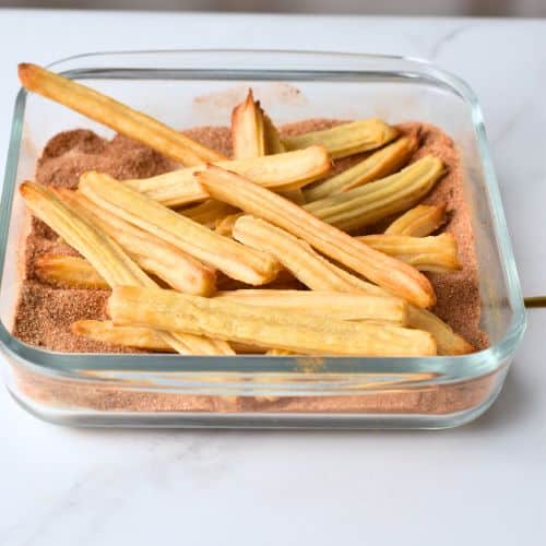 Placing baked churros in the cinnamon mixture.
